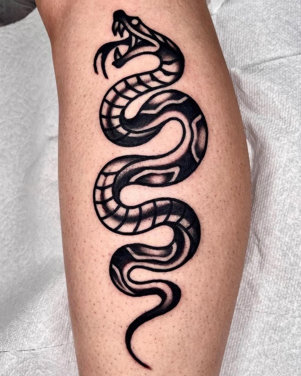 A black and grey traditional snake tattoo winding vertically down a person's shin.