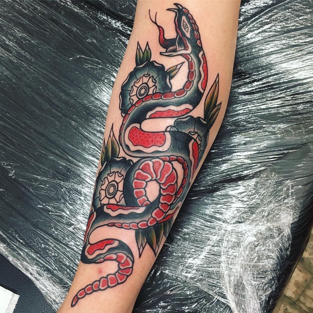 A traditional coiled snake tattoo with red and black ink on a person's shin.