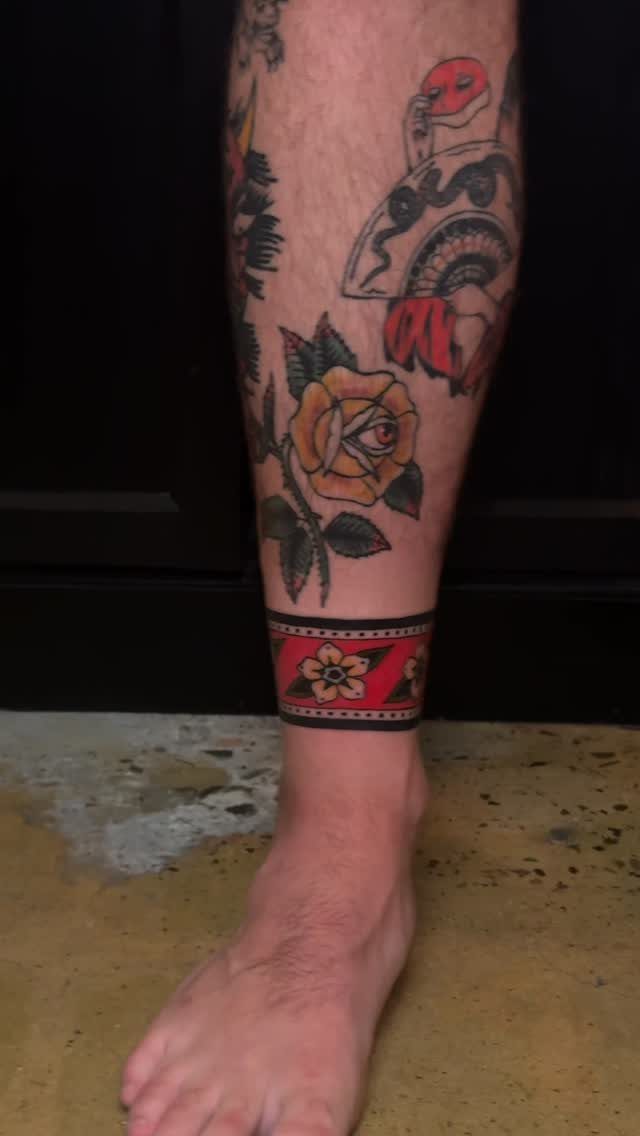 Traditional Tattoo Band: 7 Design Ideas for Arms and Legs 7 A person's lower leg showing traditional tattoos including a red and black patterned band around the ankle.