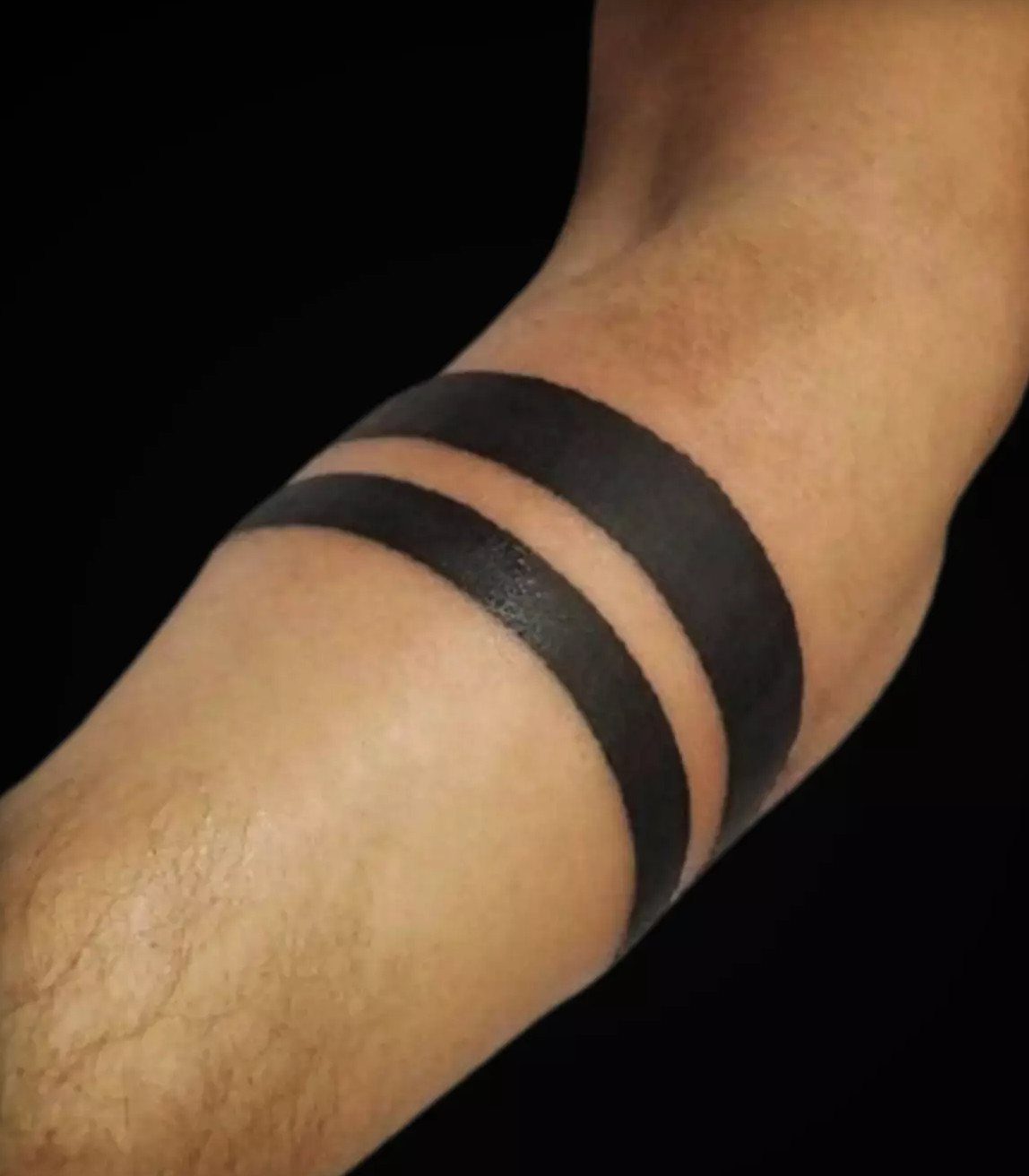 Traditional Tattoo Band: 7 Design Ideas for Arms and Legs 4 Two thick solid black parallel bands tattooed around a person's arm against a black background.