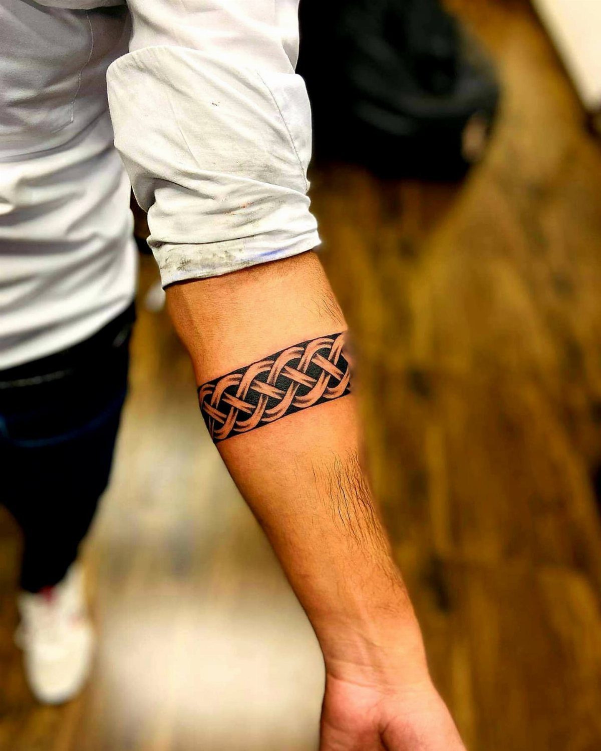 Traditional Tattoo Band: 7 Design Ideas for Arms and Legs 3 A person's forearm displaying an intricate orange and black Celtic knotwork band tattoo.