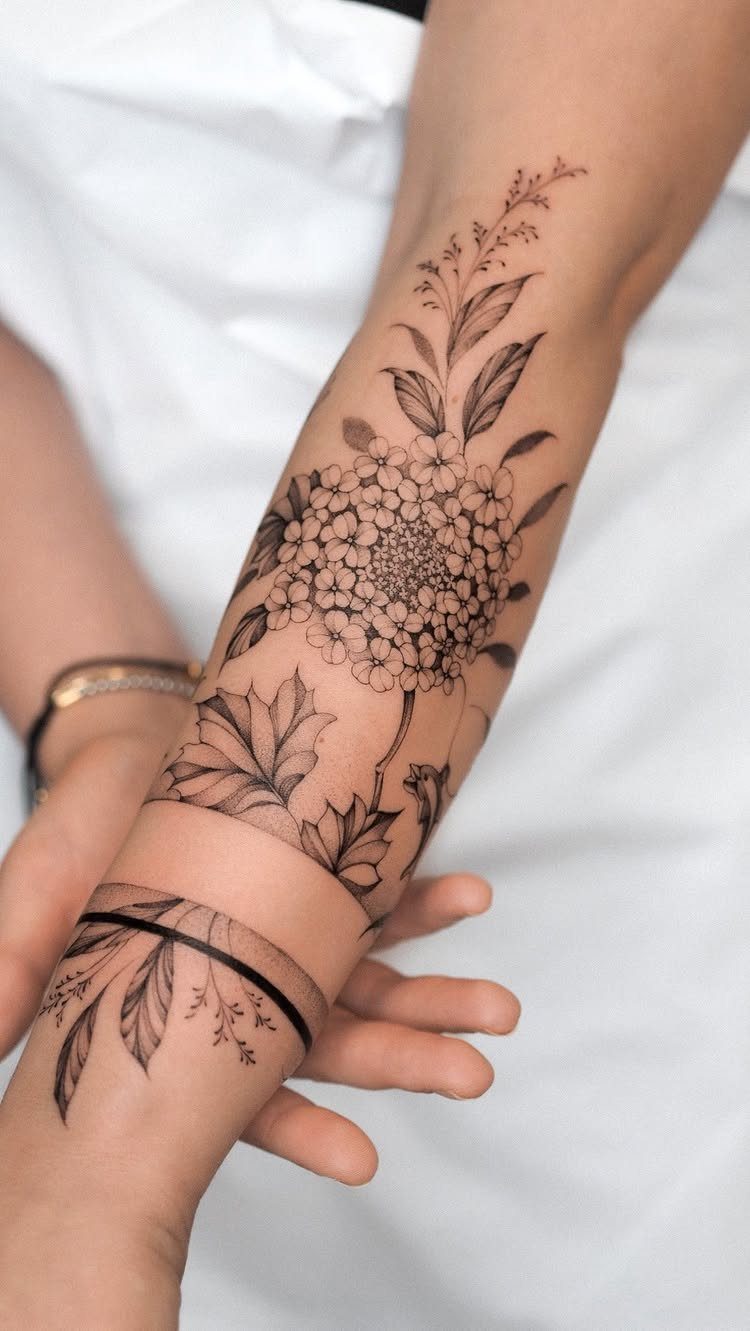 Traditional Tattoo Band: 7 Design Ideas for Arms and Legs 1 A forearm displaying a large floral tattoo and a delicate leaf band tattoo in black ink.