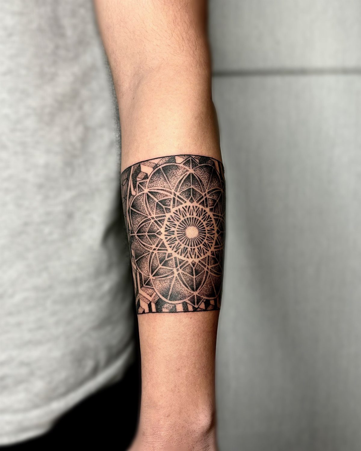 Traditional Tattoo Band: 7 Design Ideas for Arms and Legs 6 A detailed black ink geometric mandala band tattoo wrapped around a person's forearm.