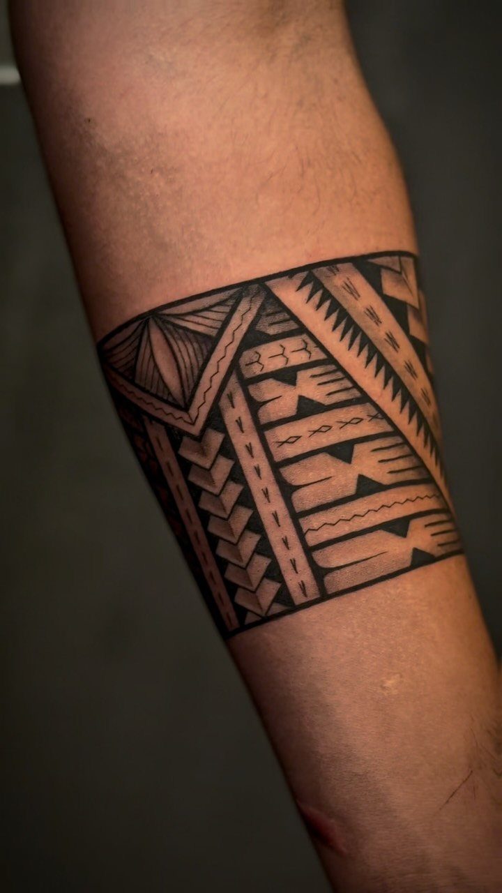 Traditional Tattoo Band: 7 Design Ideas for Arms and Legs 2 A black ink tribal band tattoo with geometric patterns wrapped around a person's arm.