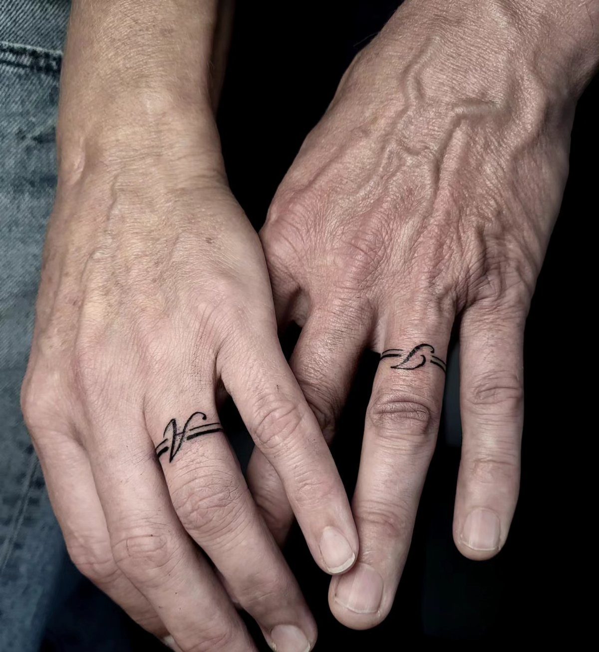 Traditional Tattoo Band: 7 Design Ideas for Arms and Legs 5 Two hands held together, each featuring a simple black line band tattoo on the ring finger.