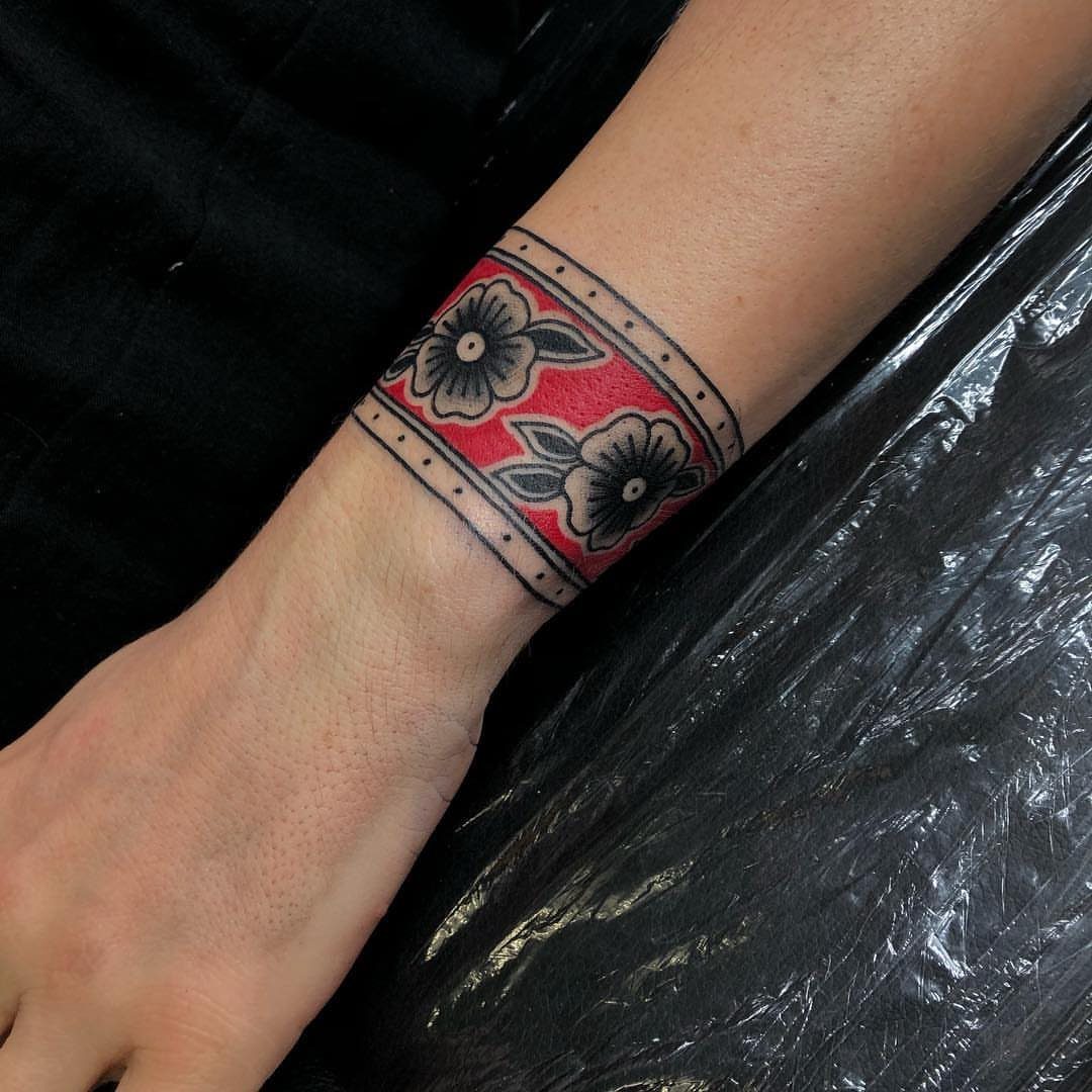 8 Traditional Tattoo Cuff Ideas for Wrists and Forearms 5 A wrist featuring a traditional red and black floral cuff tattoo design.