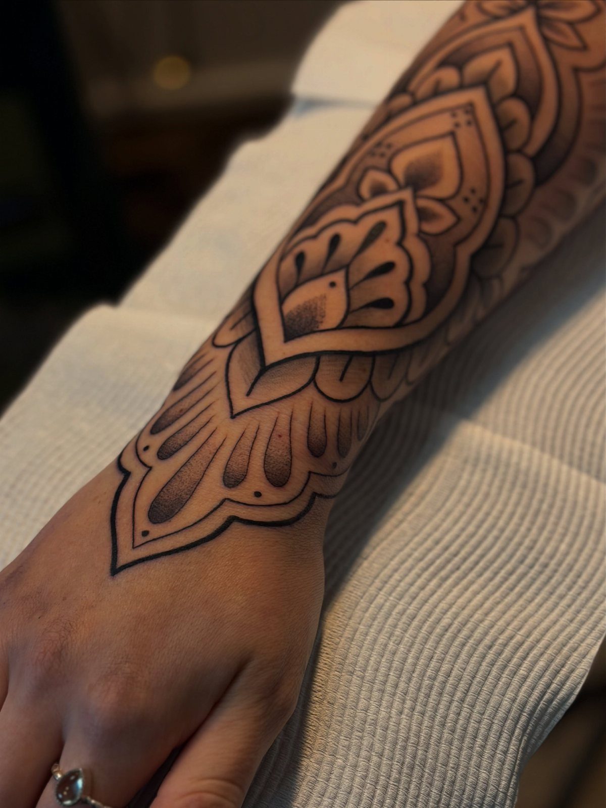 8 Traditional Tattoo Cuff Ideas for Wrists and Forearms 3 A detailed black and grey mandala pattern tattoo wrapping around a person's forearm and wrist.