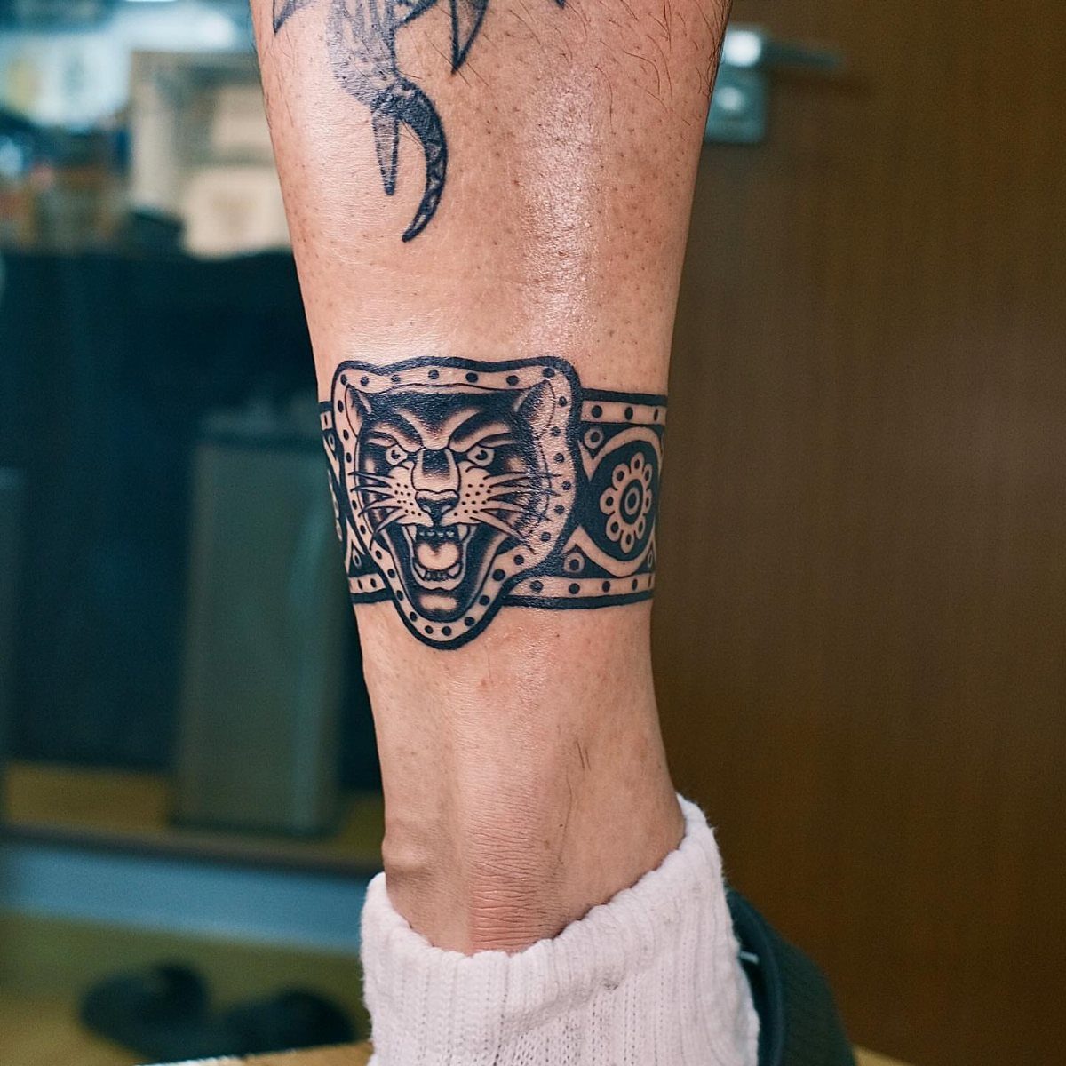 8 Traditional Tattoo Cuff Ideas for Wrists and Forearms 4 A black ink traditional panther head tattoo wrapped around a person's ankle.