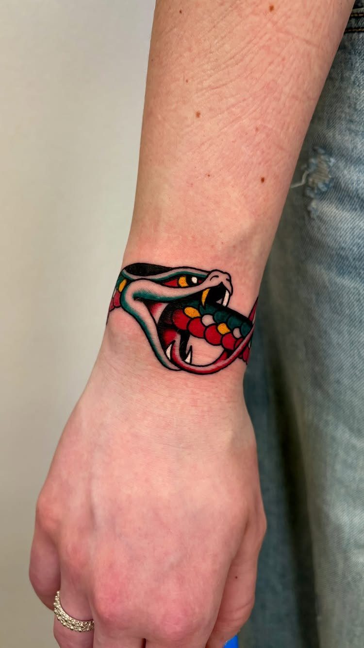 8 Traditional Tattoo Cuff Ideas for Wrists and Forearms 6 A traditional snake head tattoo wrapped around a person's wrist with bold colors.