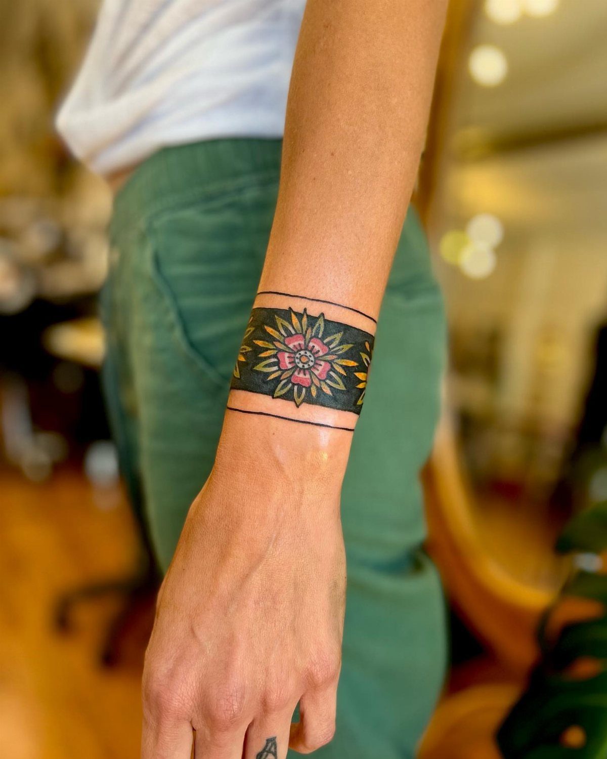 8 Traditional Tattoo Cuff Ideas for Wrists and Forearms 1 A person's wrist featuring a black band tattoo with a pink and yellow floral design.